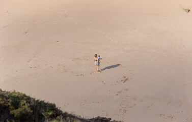 Aerial rear view of woman carrying baby while walking on the beach towards the ocean