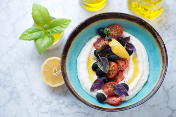 Turquoise bowl with greek meze made of fish roe or taramosalata, high angle view on a light-grey marble background