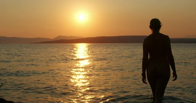 Naked girl swims at sunset on Krk island, Adriatic Sea in Croatia