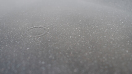 few raindrops fall in puddle on asphalt