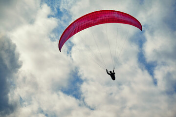 Paraglider in flight. Red paraglider in the cloudy sky
