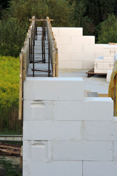 A steel reinforcement  for pillars on the first floor of a house under construction, a wooden falsework for a  reinforced concrete band, walls made of cellular concrete