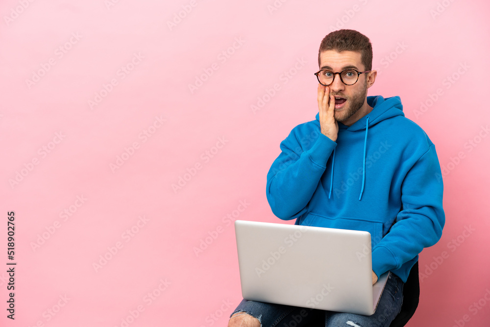 Sticker Young man sitting on a chair with laptop surprised and shocked while looking right