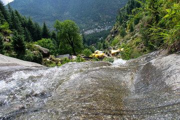 View from top of a waterfall, water is flowing below and a small village surrounded by forest can...