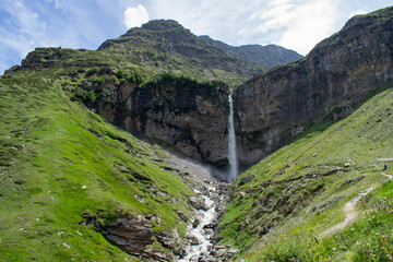 Mighty Sissu waterfall falling with all the force in Lahaul valley, Himachal Pradesh. Waterfall falling from rocky mountain. Waterfall surrounded by Green mountains and clear skies on a pleasant day.