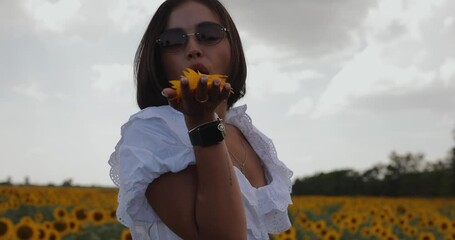 Beautiful woman blowing petals in sunflower field, slow motion