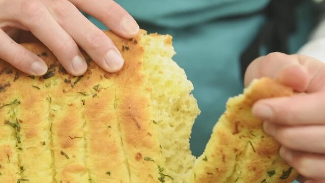 Female hands breaking freshly baked garlic bread, slow motion.
