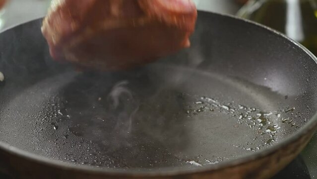 Chef preparing pork chop in a frying pan.
