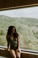 Foto op Canvas Young woman in wellness spa center sitting by the huge wide window enjoying the green forest view © BGStock72