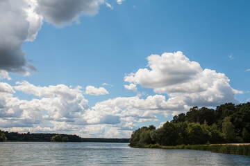 Picturesque landscape with a cloudy sky and a wide river. In the distance, across the river, there is a forest. An image as a background for your travel and nature illustrations.