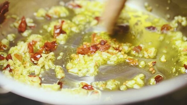 Frying and stirring of garlic and chilli pepper in a frying pan with olive oil.
