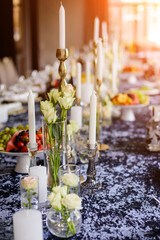 White candles in candelabra and white roses in glass vase on the wedding table decoration. 