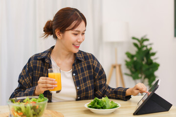 Lifestyle in living room concept, Young Asian woman pointing on tablet and drinking orange juice