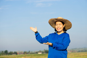 Portrait of Asian woman farmer wears hat and blue shirt, make gesture to present product for...