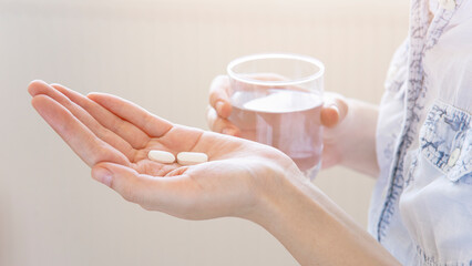 Fototapeta na wymiar Close up woman holding pill in hand with water. Female going to take tablet from headache, painkiller, medication drinking clear water from glass. Healthcare, medicine, treatment, therapy concept