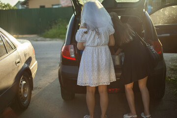 Bride is in parking lot. Bridesmaids at car dealerships. Trunk of car. Girls are getting ready for trip.