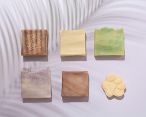 Handmade soap bars with organic ingredients on purple background in the shade of a palm leaf. Homemade beauty products with natural essential oils from plants and flowers. Body care, aromatherapy.