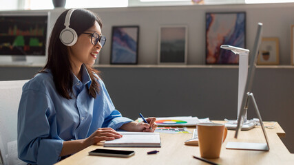 Asian Lady Working Online On Computer Taking Notes At Workplace