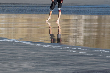 A person is standing on the wet sand, the water is rippling behind them.