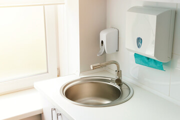 Private modern hospital ward, hand washing sink, automatic dispenser with soap, paper towels, natural light condition. Close-up shot.