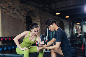 Asian man and woman exercise training in fitness gym. Young male trainer using tablet for schedule exercise training to fitness female. Workout training in fitness gym.