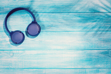 Blue headphones on blue wooden background. Wireless headphones on a pastel wooden table. Flat lay top view with copy space. Minimal style with colorful wood backdrop. Mobile streaming music concept.