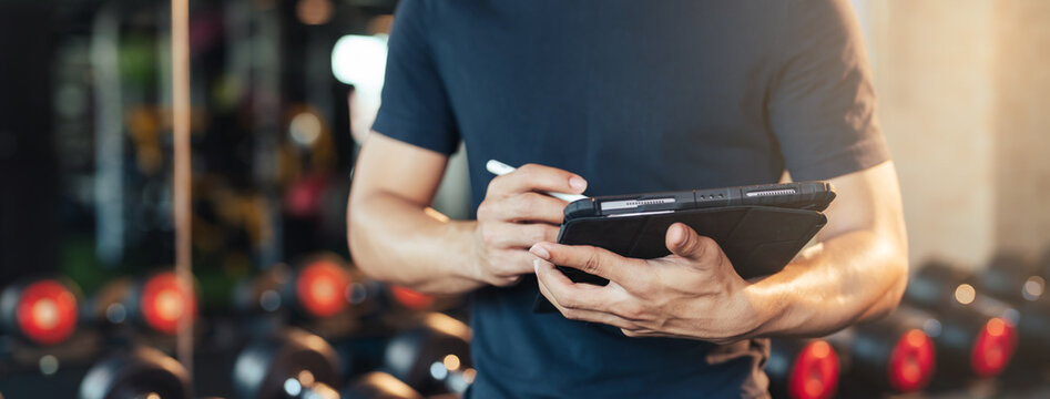 Selective focus. Hand of trainer holding and using tablet for schedule exercise training. Workout training in fitness gym.
