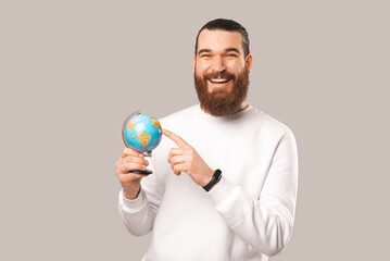 A photo of a young smiling man showng something on the globe while looking at the camera