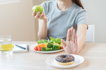 Fototapeta na wymiar Diet, Dieting asian young woman or girl use hand push out, deny sweet donut and choose green salad vegetables, eat food for good healthy, health when hungry. Close up female weight loss person.