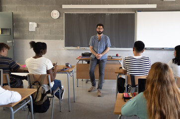 Male teacher explaining the class lesson in a classroom with multi-ethnic students. Education in...