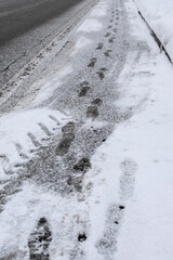 Footprints on fresh white snow at sidewalk. Asphalt covered with snow in winter season. Selective focus