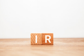 投資家向け広報。IR。インベスター・リレーションズ。木製のブロックに描かれているIRの文字。木製のテーブルの背景。