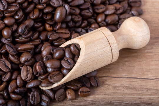 Roasted black coffee beans with a wooden spoon spilling onto the table.