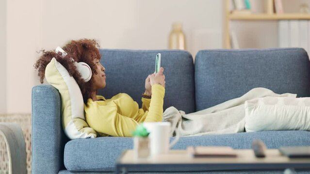 Woman listening to music with headphones relaxing and moving to the beats. Funky young African American student relaxing in her living room. Finding your favorite song while taking a study break
