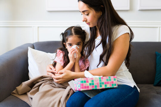 Kid with a cold blowing her nose while hugging her mother