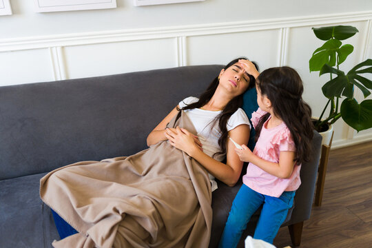 Caring kid looking after her sick mom with a faver on the sofa