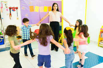 Cheerful playful teacher holding hands in a circle with her students