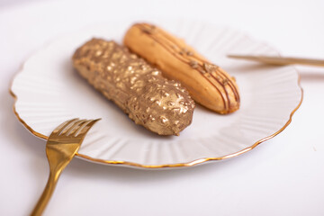 
Beautiful golden colored eclairs on plate, with knife and fork, on white background
