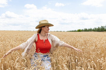 Naklejka na ściany i meble woman in a hat sitting in a field of yellow wheat field. happy woman walking in nature.
