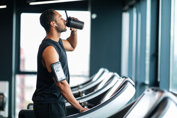 Handsome Black Male Athlete Drinking Water While Training At Treadmill At Gym