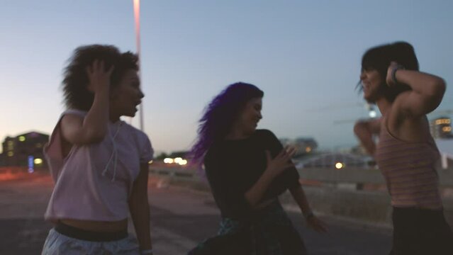 Group of funky friends dancing and having fun outside on an urban city bridge at night. Cheerful and trendy female hip hop dancers with rhythm showing off choreography moves in a dance battle