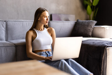 Portrait of young woman looking at camera while using her laptop at home.