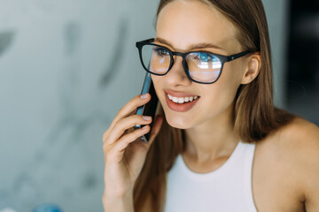 Cheerful young woman talking on the phone in the kitchen