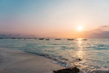 Photo sur Plexiglas Plage de Nungwi, Tanzanie NUNGWI, Zanzibar. Beau coucher de soleil sur la plage en Tanzanie, Afrique. Mer turquoise, ciel orangé. Bateaux de pêche à l& 39 horizon.