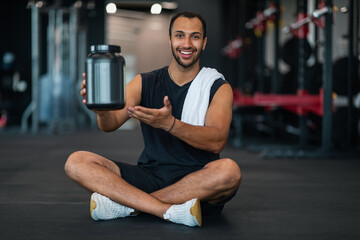 Fototapeta na wymiar Smiling Sporty Black Man Demonstrating Container With Whey Protein Powder At Camera