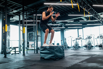 Fototapeta na wymiar Motivated black male athlete doing balance exercise on cube in modern gym