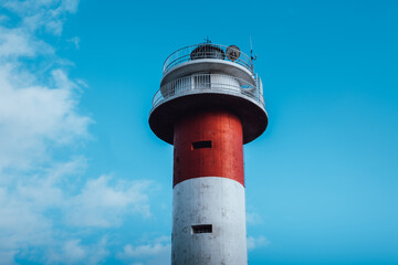 Detail of a white and red lighthouse on a sunny day with clouds