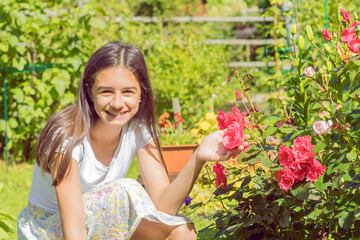 Smiling pretty teenage girl in a summer garden near a blooming rose bush.