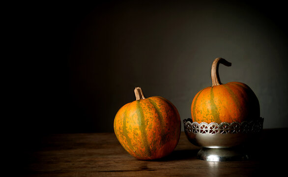 Still life of two small pumpkins. Minimalism. Simplicity. Warm colors. Dark background