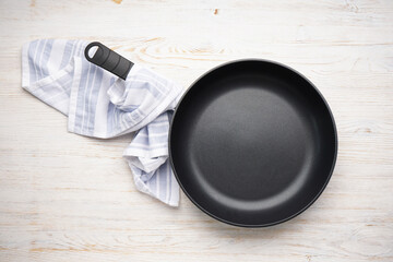 New frying pan and kitchen towel on a wooden background. Top view.